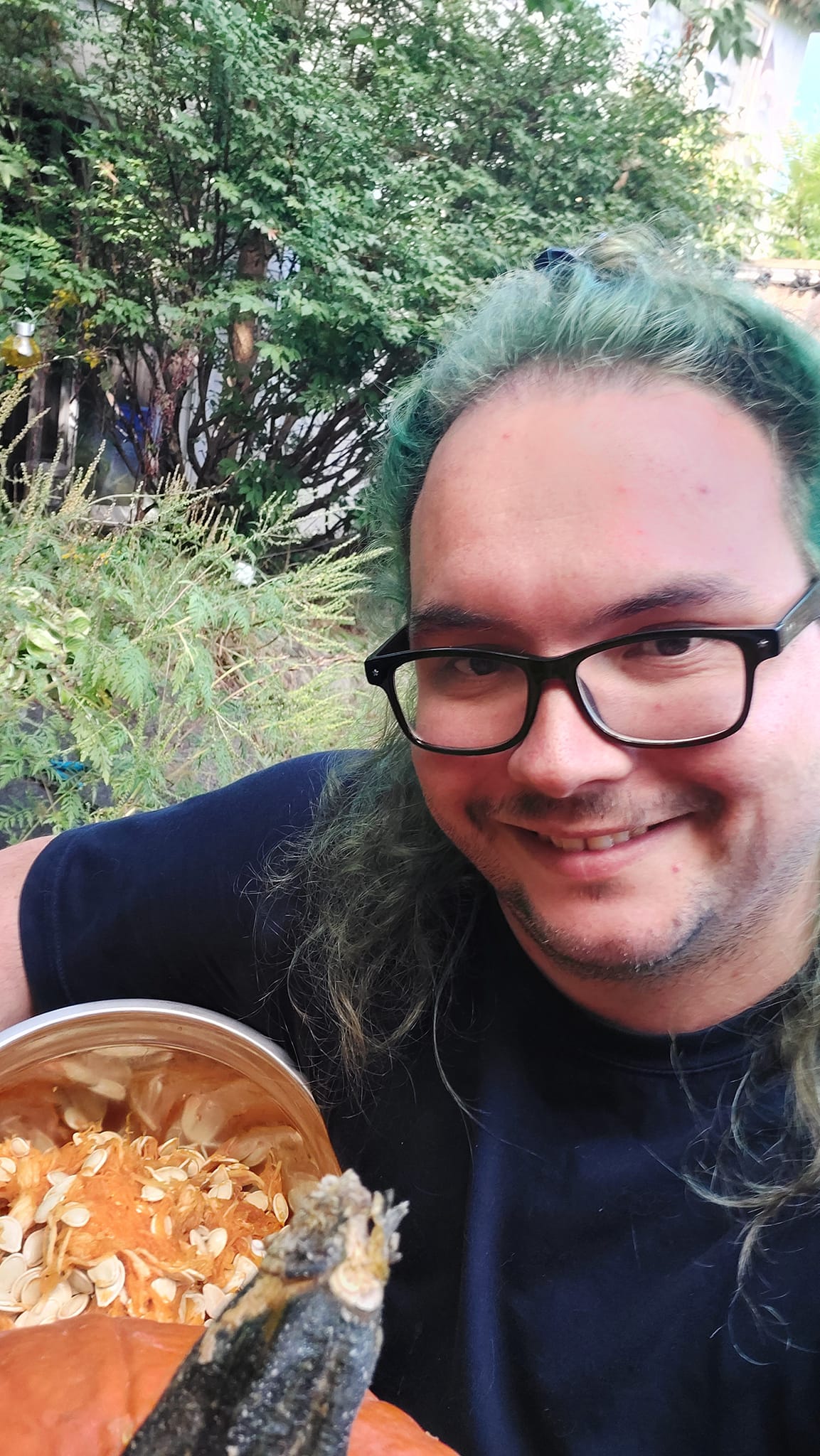 A man with long green hair and no beard holds a bowel full of pumpkin seeds